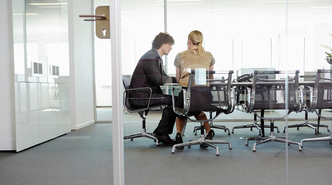 Two employees hold a meeting in a glass-partitioned office