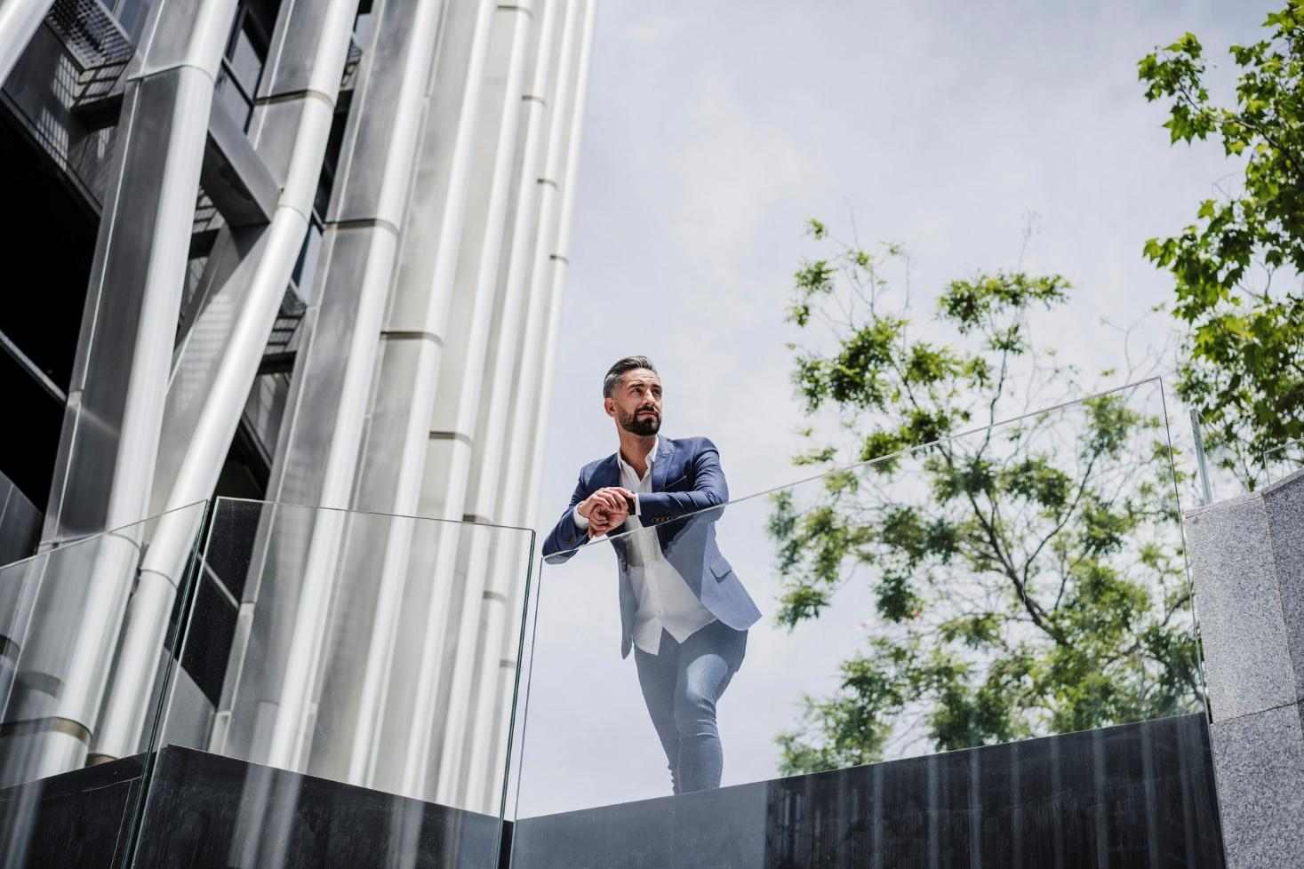 A young man is leaning on an outdoor glass railing.