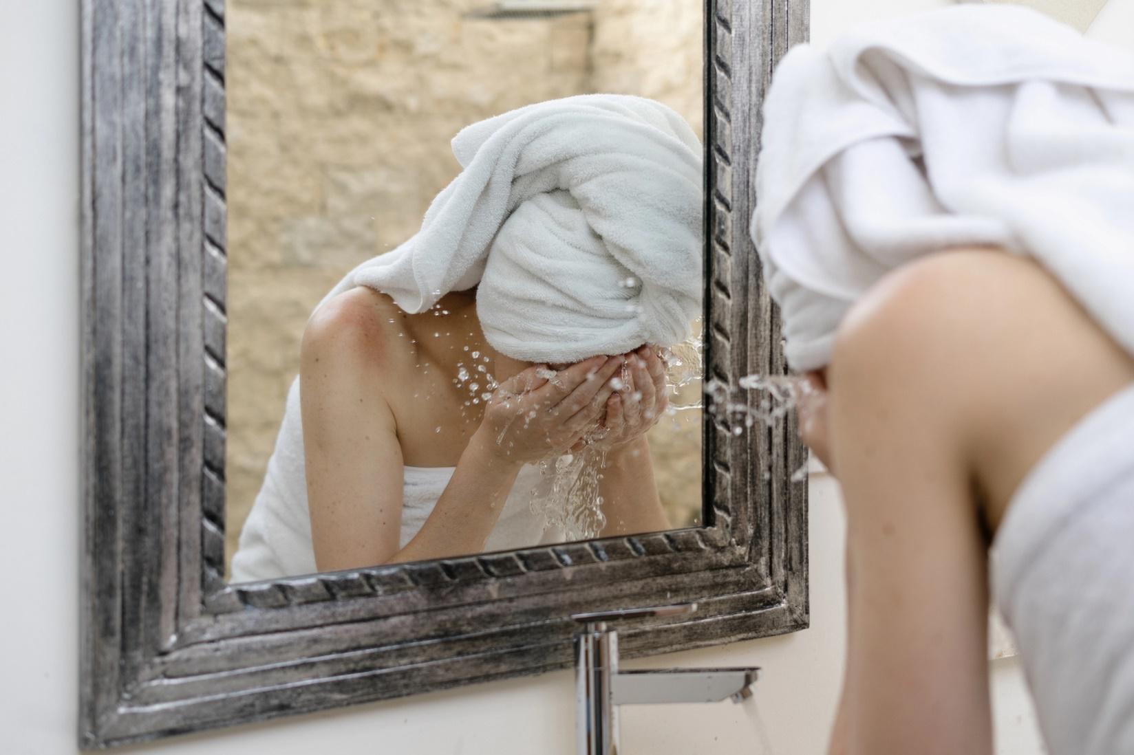 A woman washes her face in front of a mirror